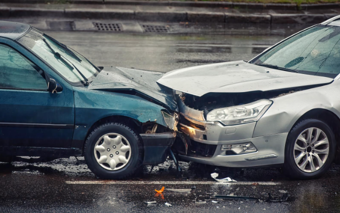 Two cars involved in a head-on collision on a wet road, showing heavy front-end damage to both vehicles.