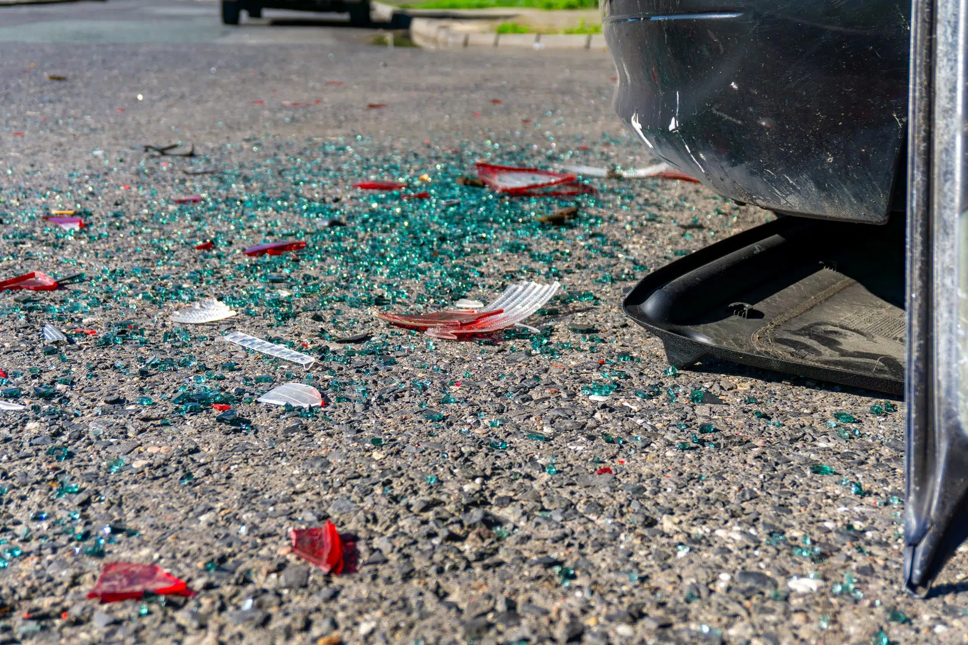 Close-up of broken glass and debris on the road next to a damaged vehicle after a car accident.