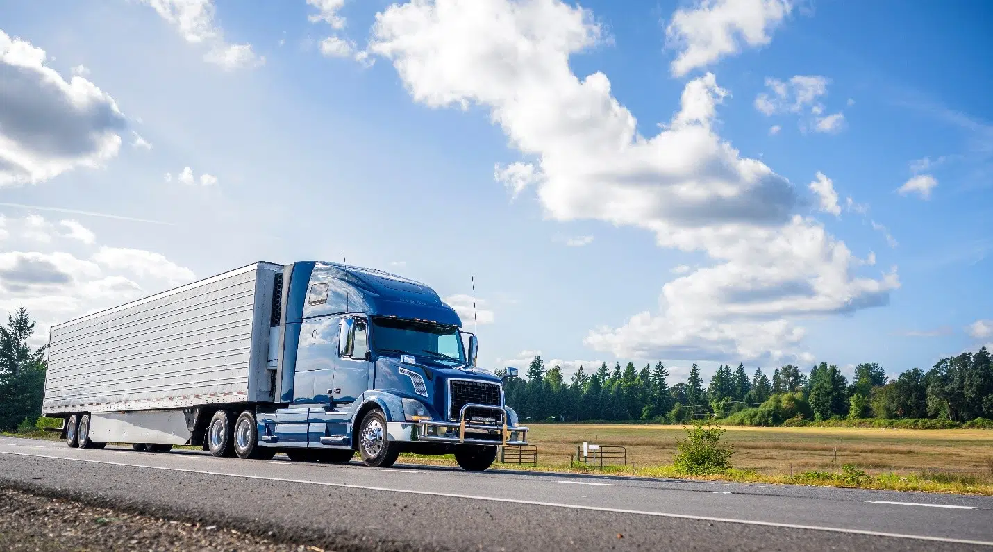 Large semi-truck driving on an open road under a blue sky, representing commercial trucking or transportation.