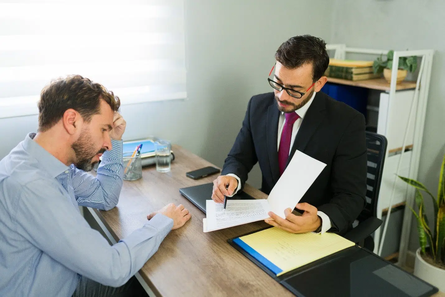 Attorney in a suit reviewing documents with a concerned client seated at a desk in an office setting.