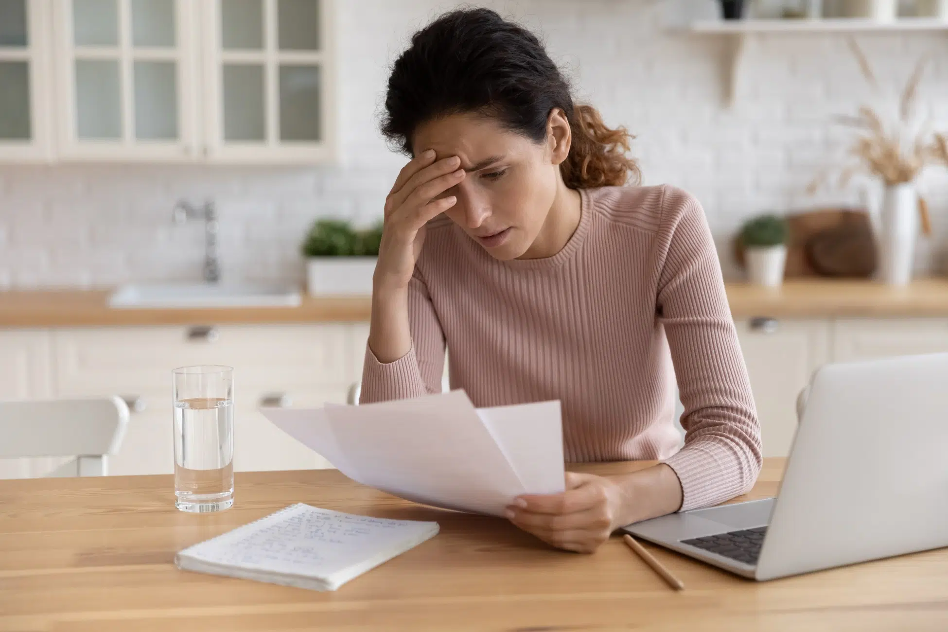 Worried woman reviewing medical bills and paperwork at her kitchen table after a personal injury
