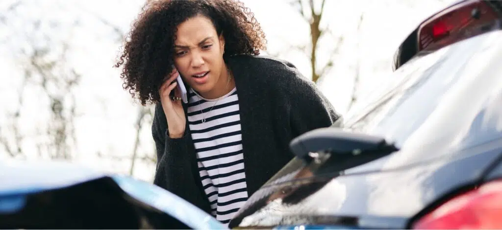 A woman talking on the phone while looking at damage from a car accident