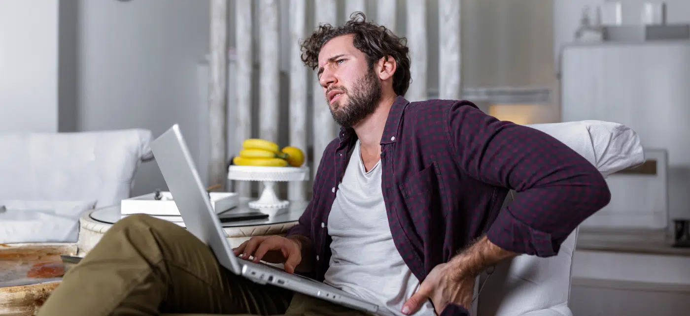 Man sitting with his laptop clutches his side in pain