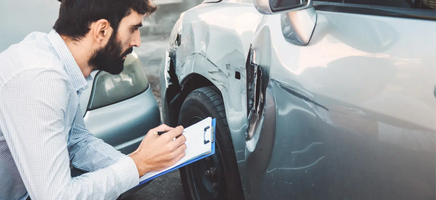 Man with clipboard examines vehicle damage