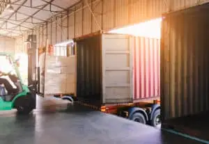 A forklift driver loading cargo into the back of a semi-truck.