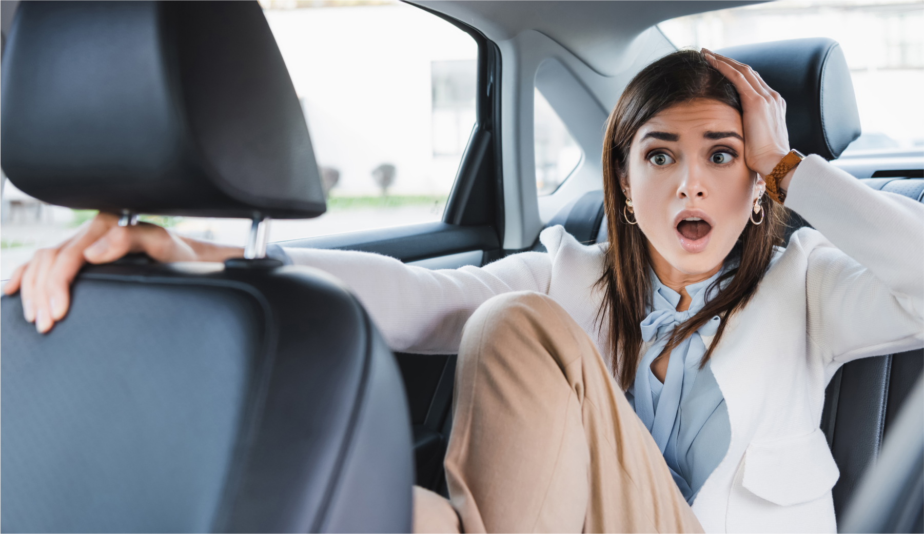 A passenger in the back of a rideshare vehicle holding onto the seat in front of her with a shocked expression