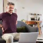A man sitting on the couch experiencing back pain