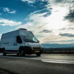White commercial vehicle transporting through highway on bright sunny sunset.