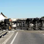 A large commercial truck lying overturned on a highway, blocking multiple lanes with debris scattered on the road.