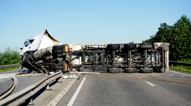 A large commercial truck lying overturned on a highway, blocking multiple lanes with debris scattered on the road.