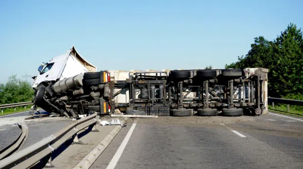 A large commercial truck lying overturned on a highway, blocking multiple lanes with debris scattered on the road.