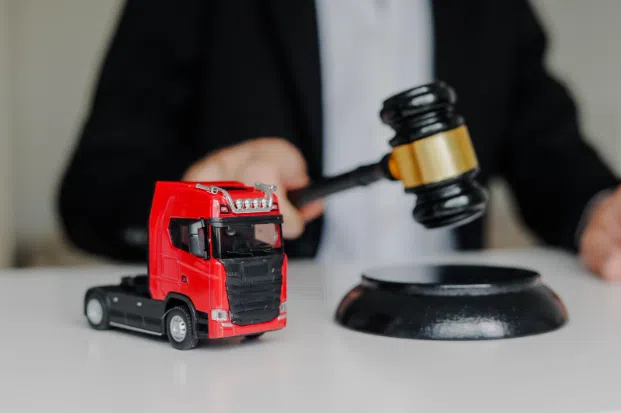 A small red toy truck placed on a white table next to a judge’s gavel, symbolizing legal action or trucking accident law.