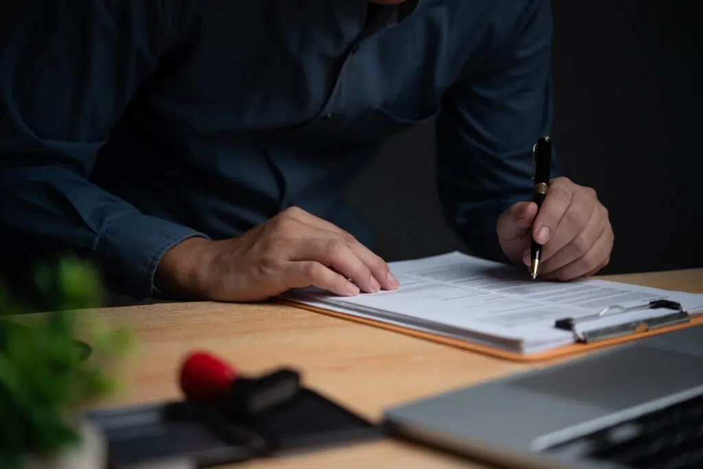 Person signing an official document on a clipboard with a pen at a desk.