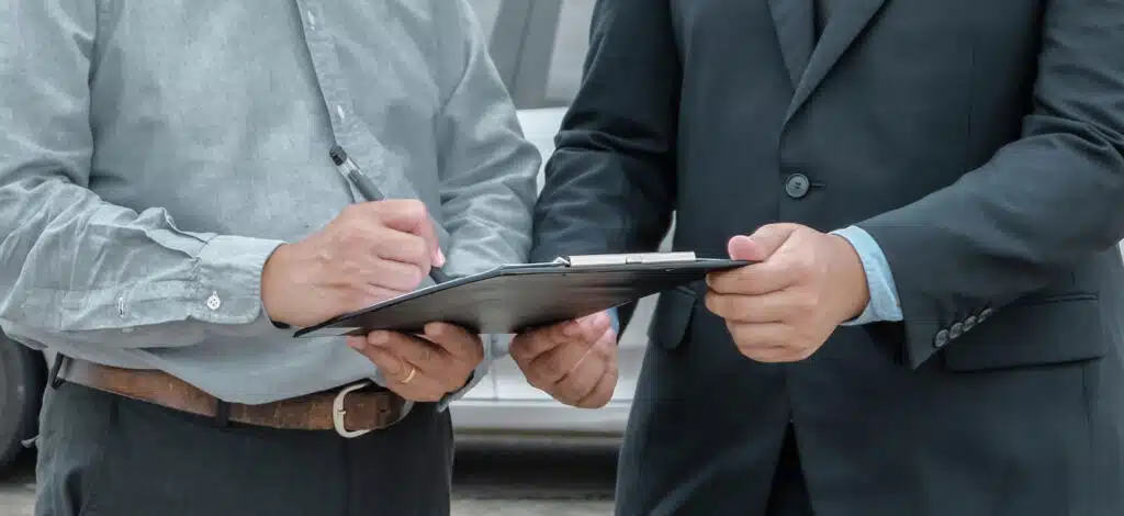 An insurance adjuster sharing paperwork on a clipboard while a car accident victim is signing the paperwork