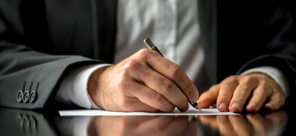 Man in a suit writing on a piece of paper with a fancy pen.