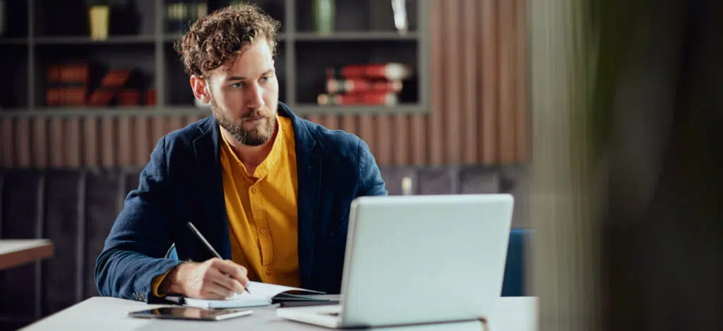 A man taking notes and looking at a laptop