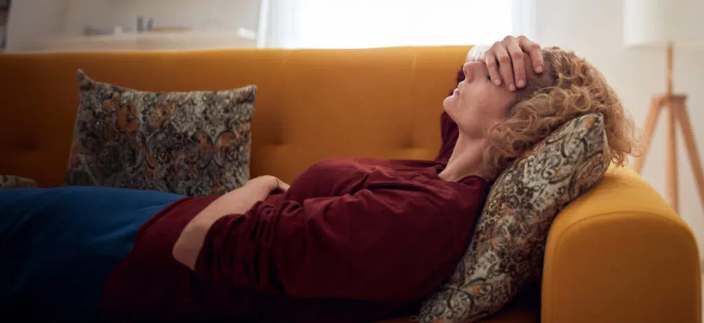 A woman lying on a couch with her hand on her forehead and eyes closed