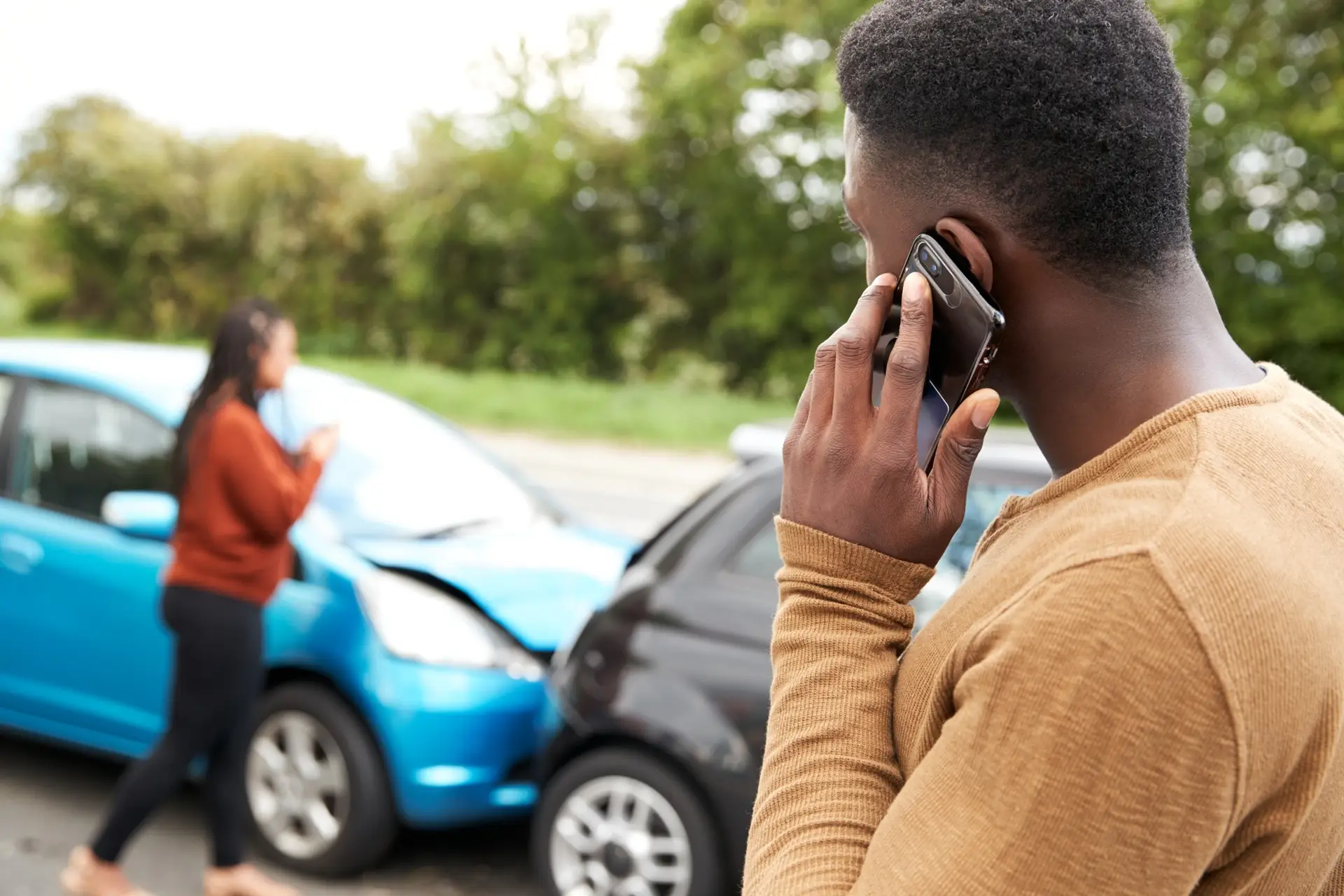 Man on the phone reporting a car accident with damaged vehicles on the roadside