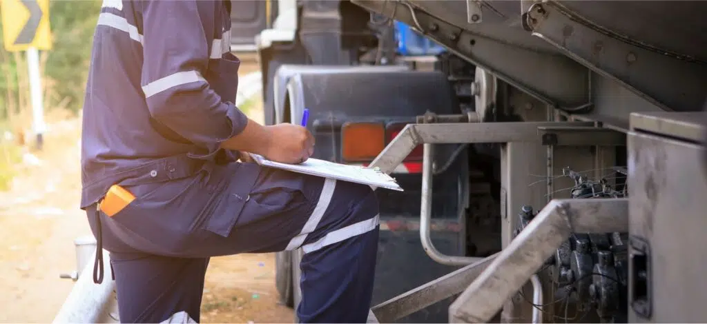A man with a clipboard examines a tractor trailer for maintenance issues.