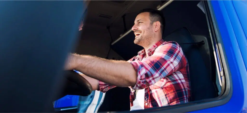 A truck driver smiles behind the wheel of his cab.