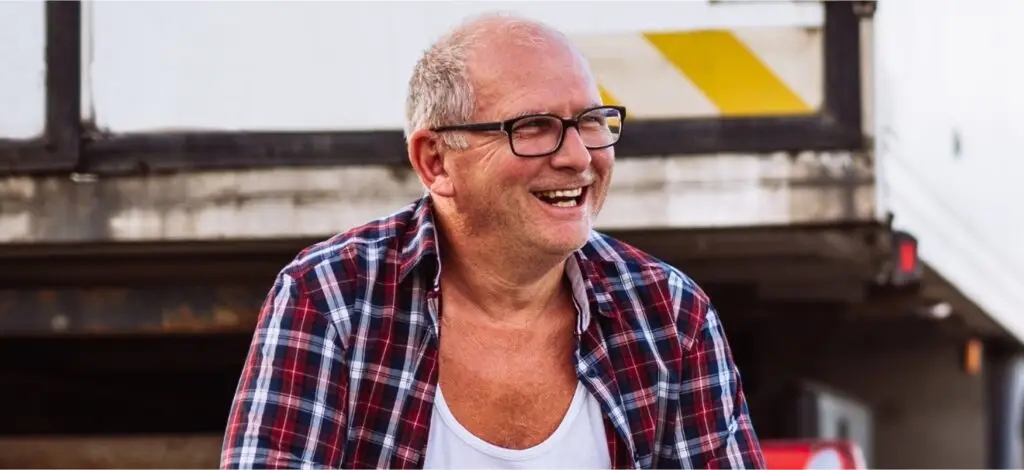 A man smiles, with a tractor trailer in the background.