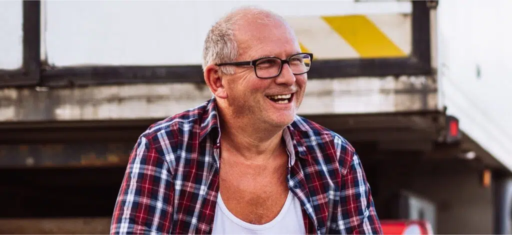 A man smiles, with a tractor trailer in the background.