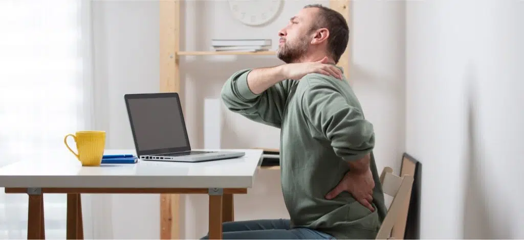 A man seated at a table showing that he has neck and back pain