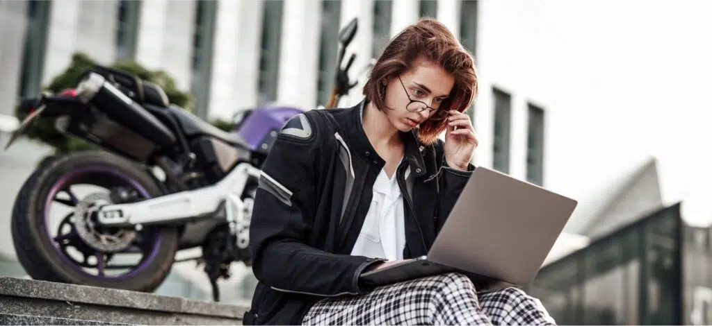 a person sitting steps reading on their computer with a motorcycle behind them