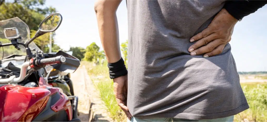 a person with back pain standing by a motorcycle on the road