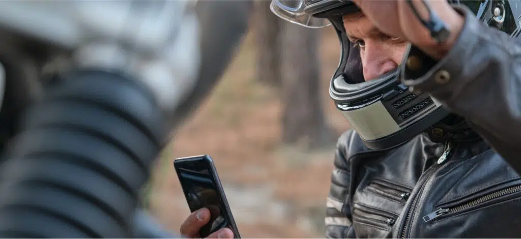 a motorcycle rider with a helmet on looking at his cell phone while stopped