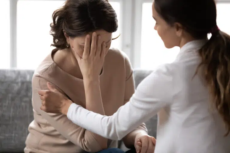 A supportive scene where one woman comforts another who is covering her face with her hand in sadness or emotional distress.