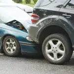 Rear-end car accident showing a blue sedan that has crashed into the back of a black SUV, depicting vehicle damage and the aftermath of a traffic collision.