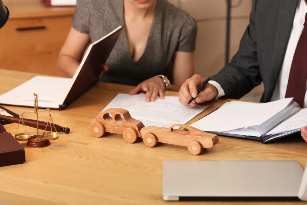 Two lawyers reviewing a car accident case at a desk with wooden toy cars, a legal scale, and documents, symbolizing auto accident law, legal advice, and personal injury claims.