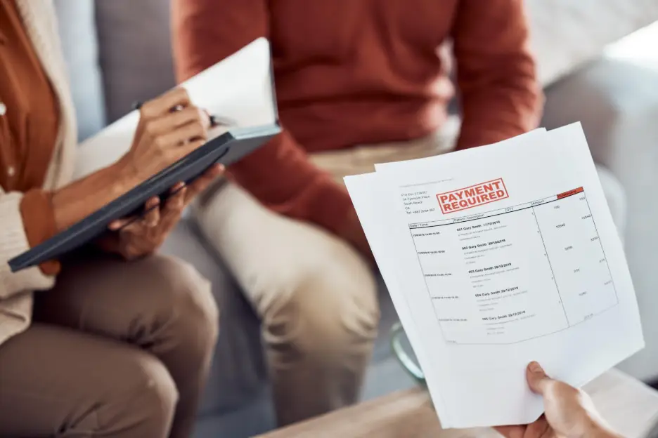 Person holding medical bills labeled “Payment Required” while another person takes notes, suggesting a discussion about healthcare or accident-related expenses.