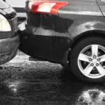 Two cars involved in a rear-end collision on a wet road, showing bumper damage and brake lights illuminated.