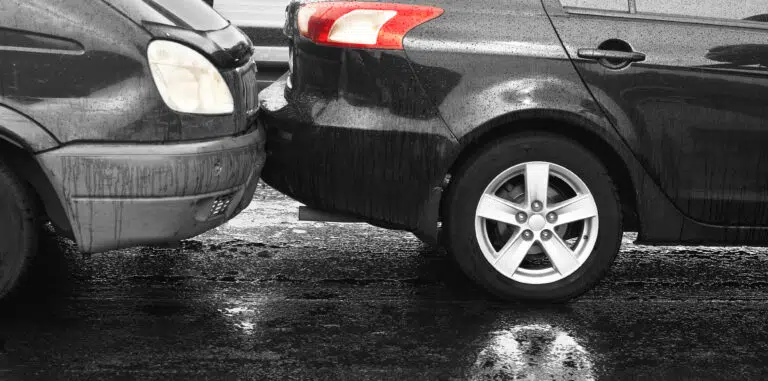 Two cars involved in a rear-end collision on a wet road, showing bumper damage and brake lights illuminated.