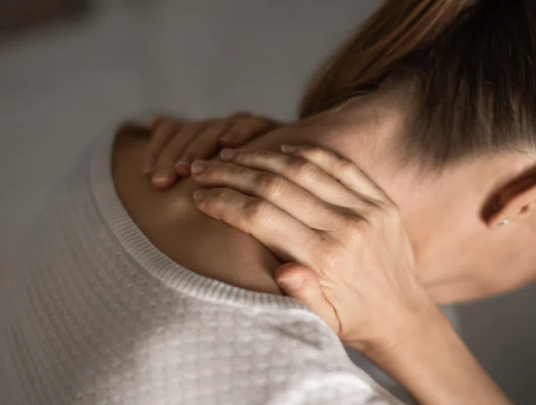 Close-up of a person holding the back of their neck with both hands, suggesting neck pain or stiffness.