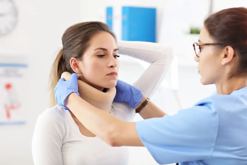 Healthcare professional wearing gloves fitting a cervical neck brace on a woman in a clinical setting.