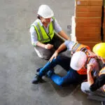 Top view. First Aid and safety first. Engineering talking on walki talki radio to employee while his warehouse coworker lying unconscious at industrial factory. Health insurance emergency accident.