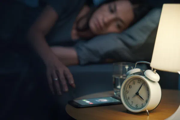 Woman lying awake in bed at night next to alarm clock showing late hour