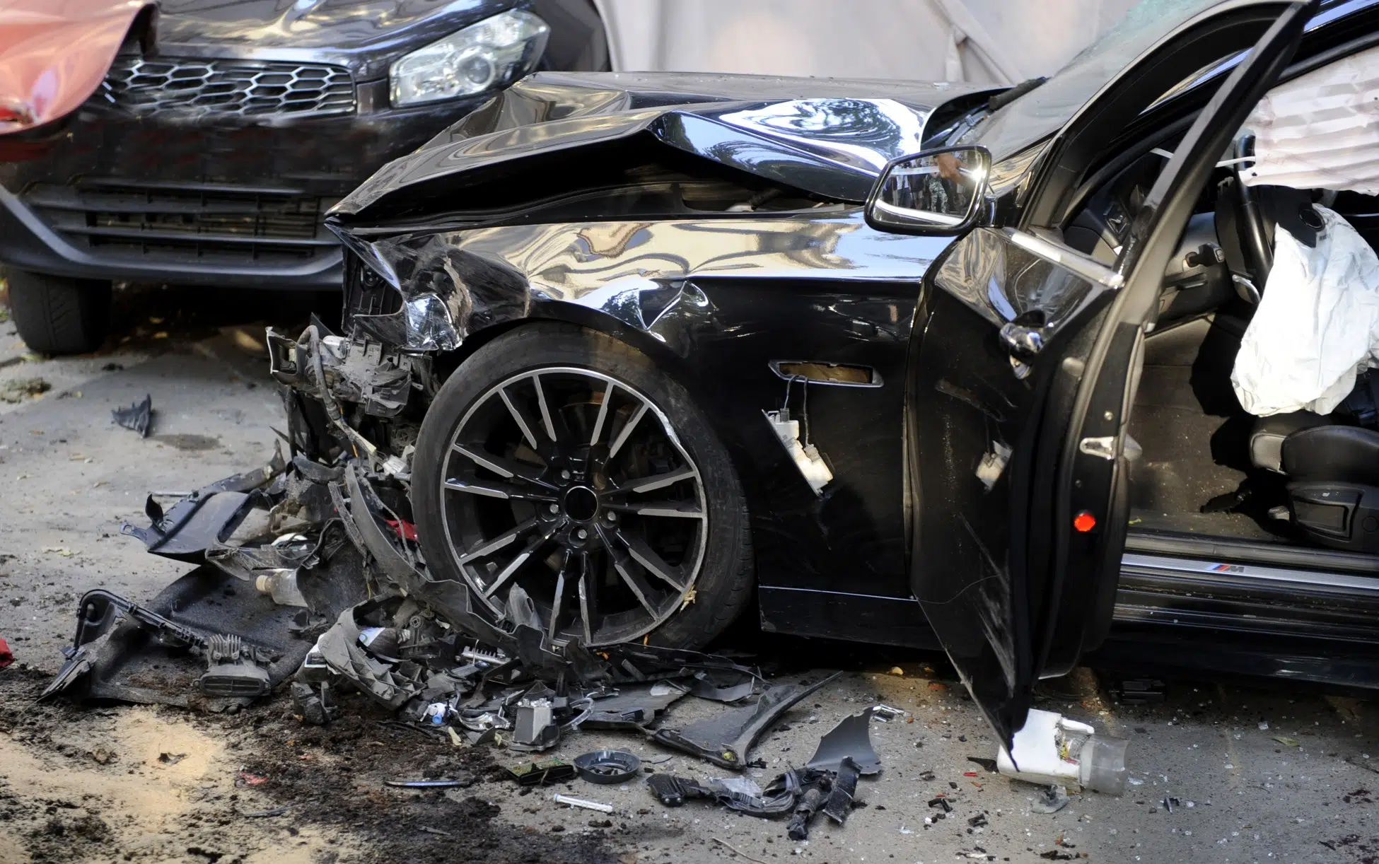 Severely damaged black sedan with deployed airbag and detached front bumper after a high-impact collision