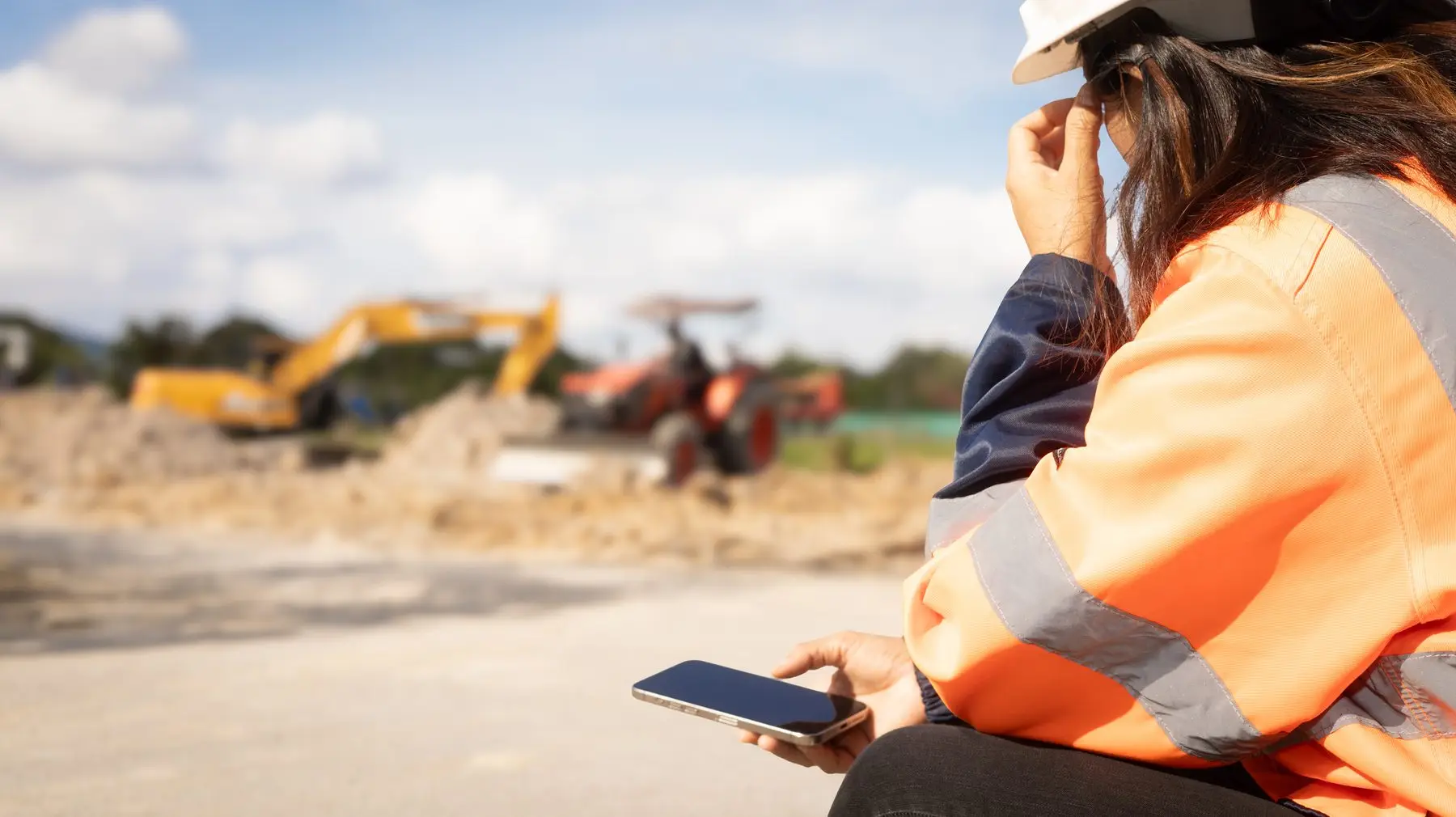 Injured worker in a hi-vis vest sitting at an Oklahoma job site holding a phone